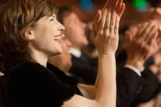 Eine Frau lächelt und applaudiert in einem begeisterten Publikum.