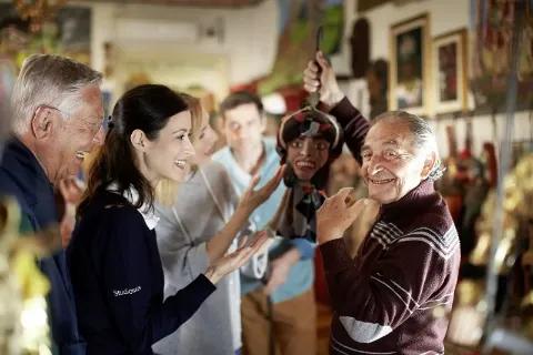 Ein älterer Mann hält eine Marionette und lächelt, umgeben von einer Reisegruppe.