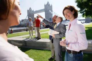Eine Reisegruppe mit Reiseleiterin, die bei sonnigem Wetter den TowerBridge in London anschauen.
