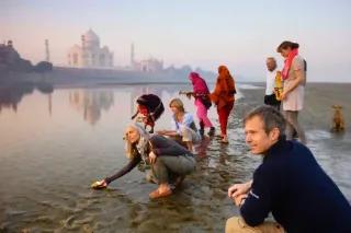 Morgenstimmung am Taj Mahal in Indien, mit Menschen, die am Ufer Blumen ins Wasser werfen.