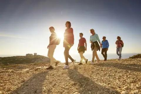 Eine Gruppe von sechs Personen wandert auf einem Bergweg bei Sonnenuntergang.