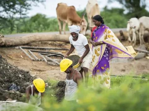 Eine Frau in einem bunten Sari beobachtet Bauarbeiten auf einem Feld.