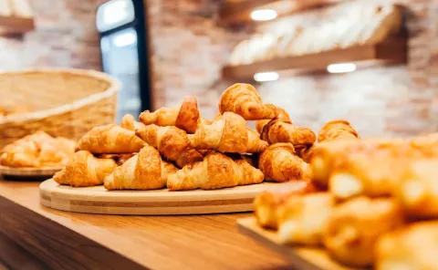Ein Stapel frisch gebackener Croissants auf einer Holzplatte in einer Bäckerei.