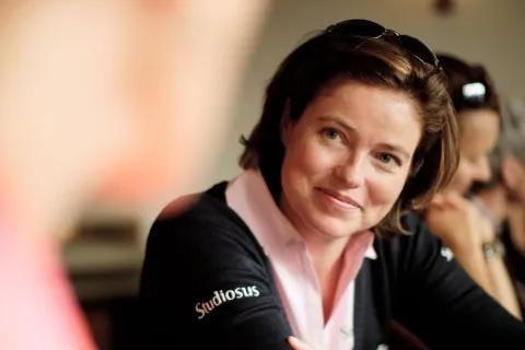 Eine Frau mit Sonnenbrille, die an einem Tisch sitzt und lächelt.