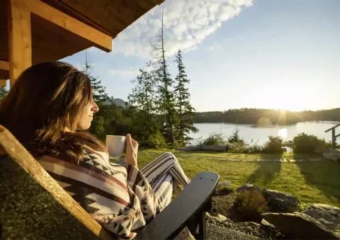 Eine entspannte Frau genießt ihren Kaffee mit Blick auf einen See bei Sonnenaufgang.