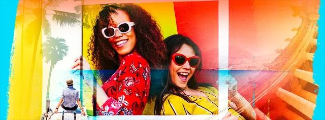 Zwei Frauen lachen und posieren mit Sonnenbrillen vor einer bunten Kulisse.