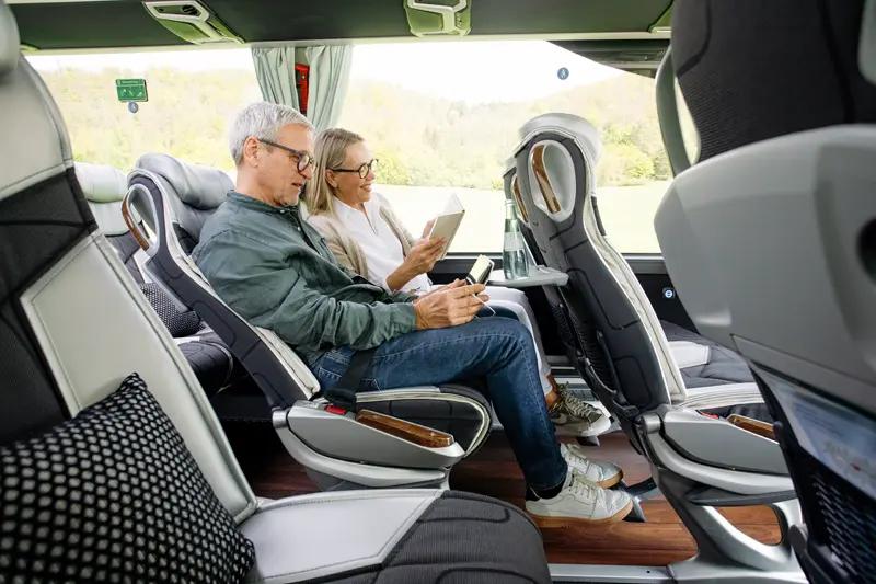 Ein Paar, das Bücher und Handys nutzt, sitzt auf bequemen Sitzen in einem Reisebus.