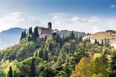 Eine Landschaft mit einem historischen Kloster, das auf einem bewaldeten Hügel thront.