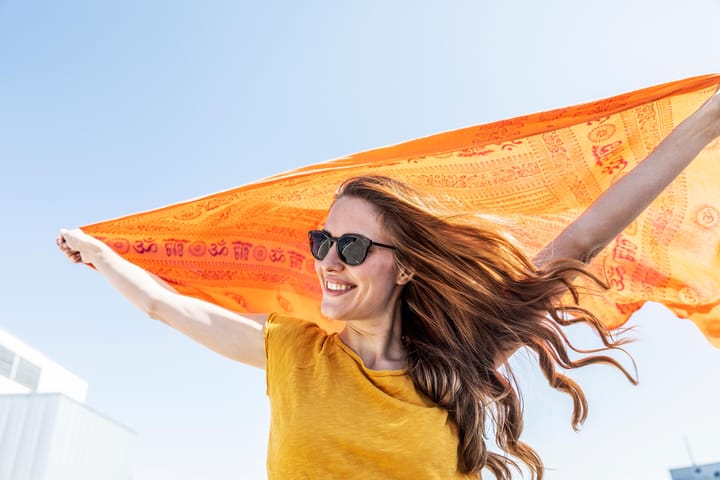 Titelbild: eine fröhliche Frau hält ein orangenes Tuch über ihren Kopf