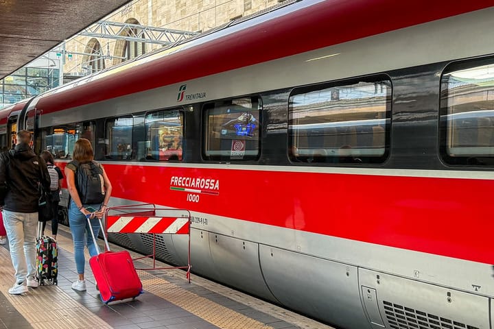 Ein italienischer Frecciarossa Zug in rot und grau hält an einem Bahnsteig.